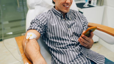 A cropped shot of a man in a striped shirt getting IV therapy while smiling at something on his phone