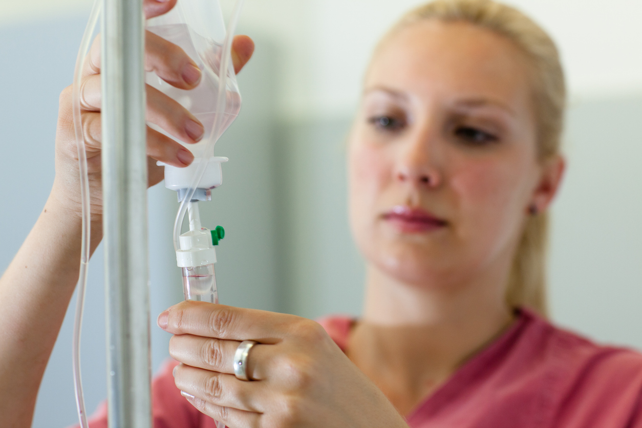 Blurred close-up of a blond woman in scrubs preparing an IV Drip