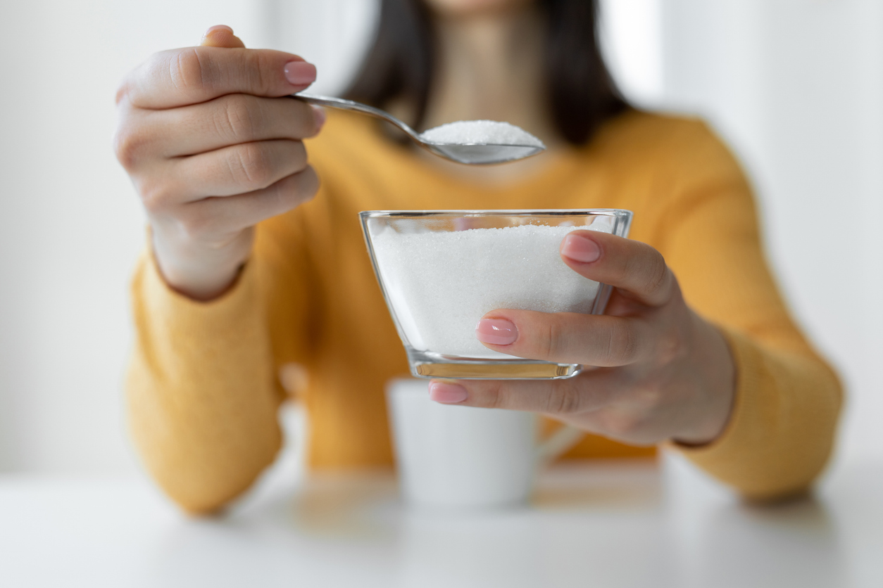 Blurred close-up of a woman holding a bowl and spoonful of sugar for coffee