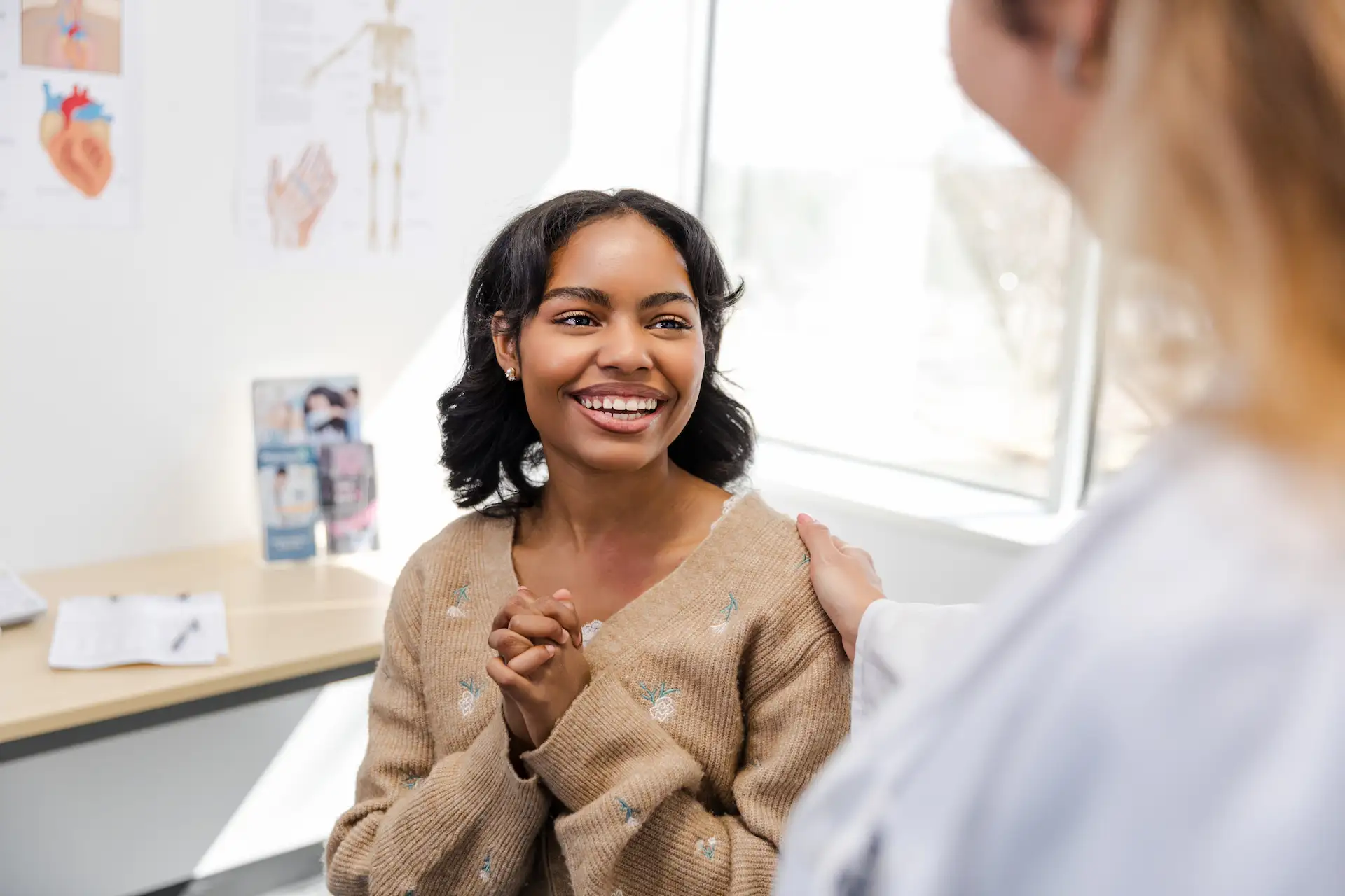 Smiling young woman with a female doctor resting her hand on the patient’s shoulder