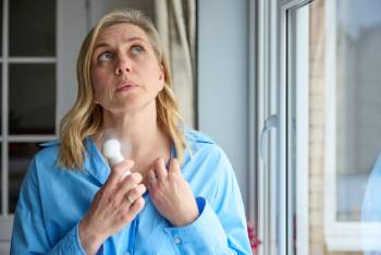 Woman having hot flash cooling herself with handheld fan