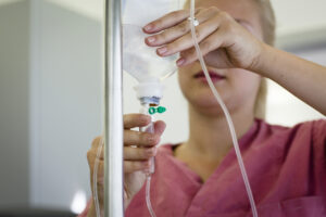 Close-up of a woman in pink scrubs holding an IV she’s setting up