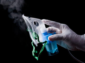 A gloved hand holding a nebulizer mask with mist coming out of it
