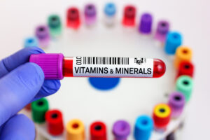 Blue gloved hand holding a blood sample tube that says vitamins and minerals on it
